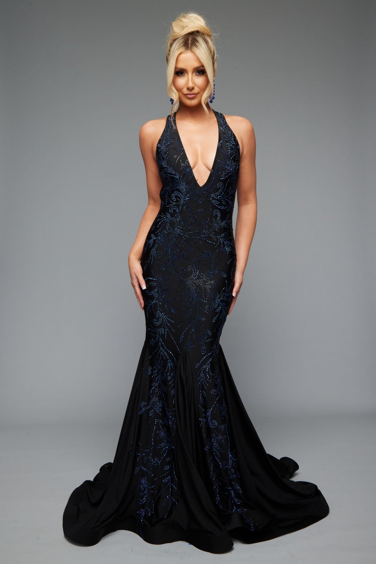 Front view of stunning black best selling fitted prom dress with a plunge neckline, open back, halter neckline, and applique design.