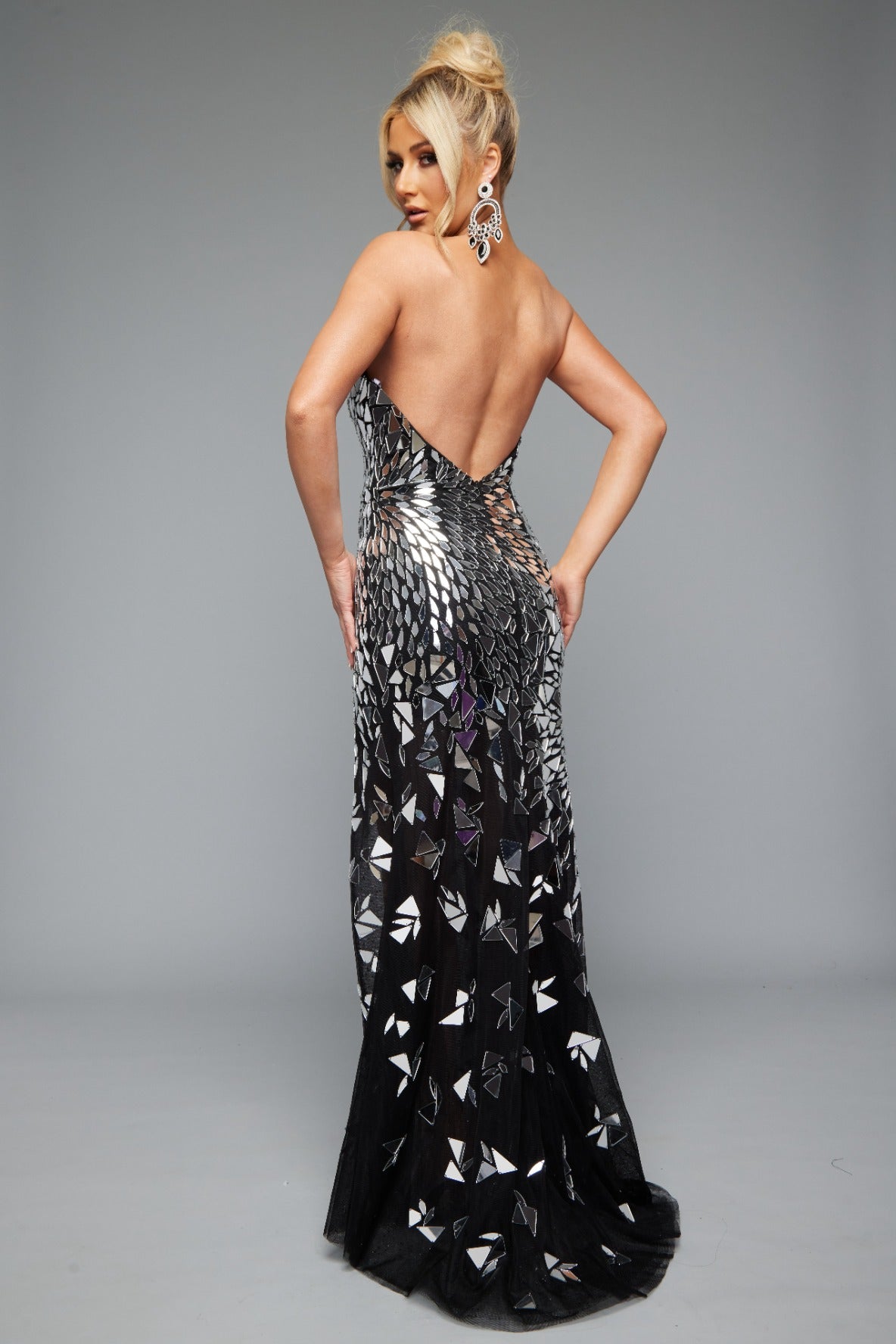Back view of a dazzling black and silver prom dress featuring a high slit, mirror accents, an open back, and a strapless, sweetheart neckline.