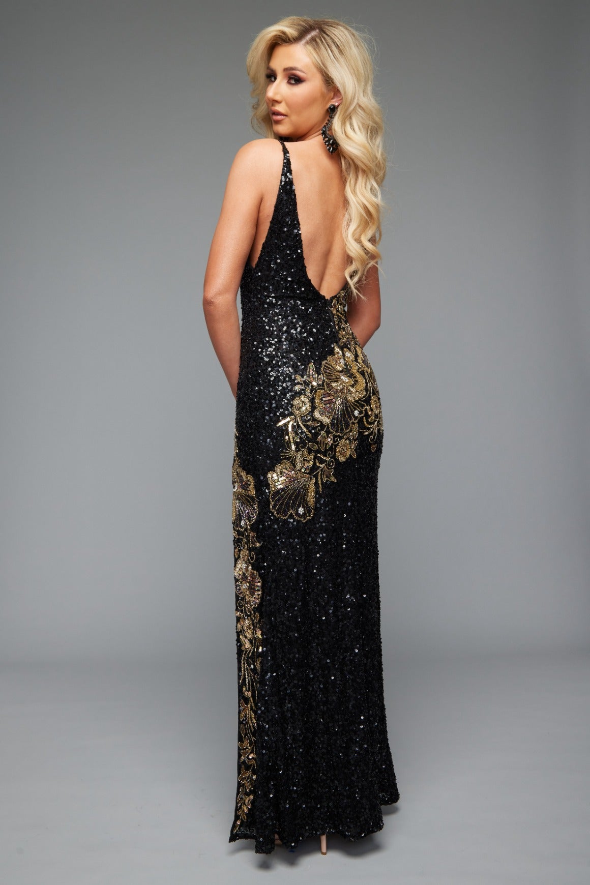 Back view of Style 7646: a captivating best selling prom dress featuring a beaded applique design, high slit, open back, plunge neckline, and spaghetti straps. Available in black and gold and a must-have for prom night.