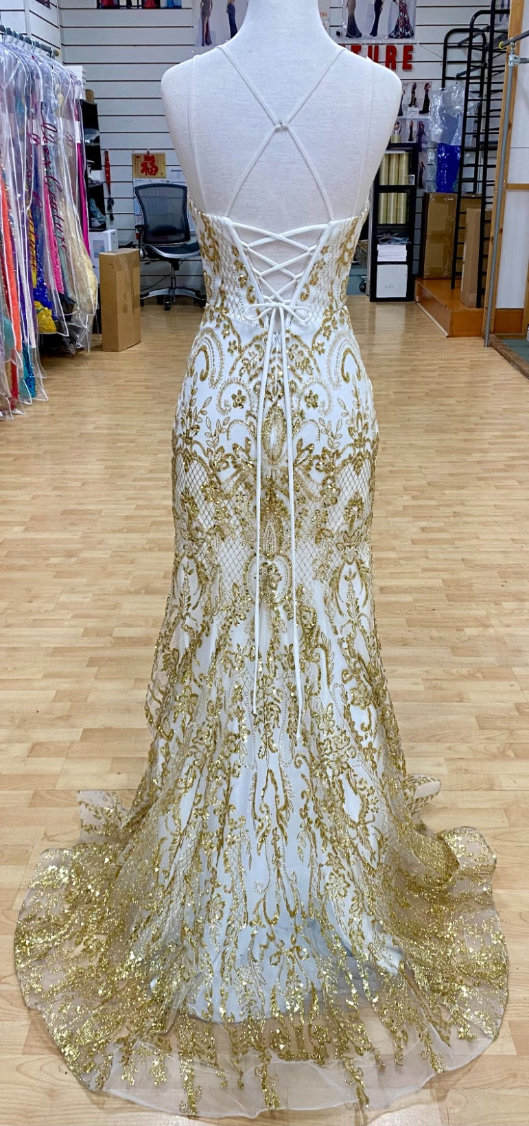 Back view of Style 7648: an eye-catching, best selling white and gold prom dress featuring an applique design, corset lace up detail, and spaghetti straps.