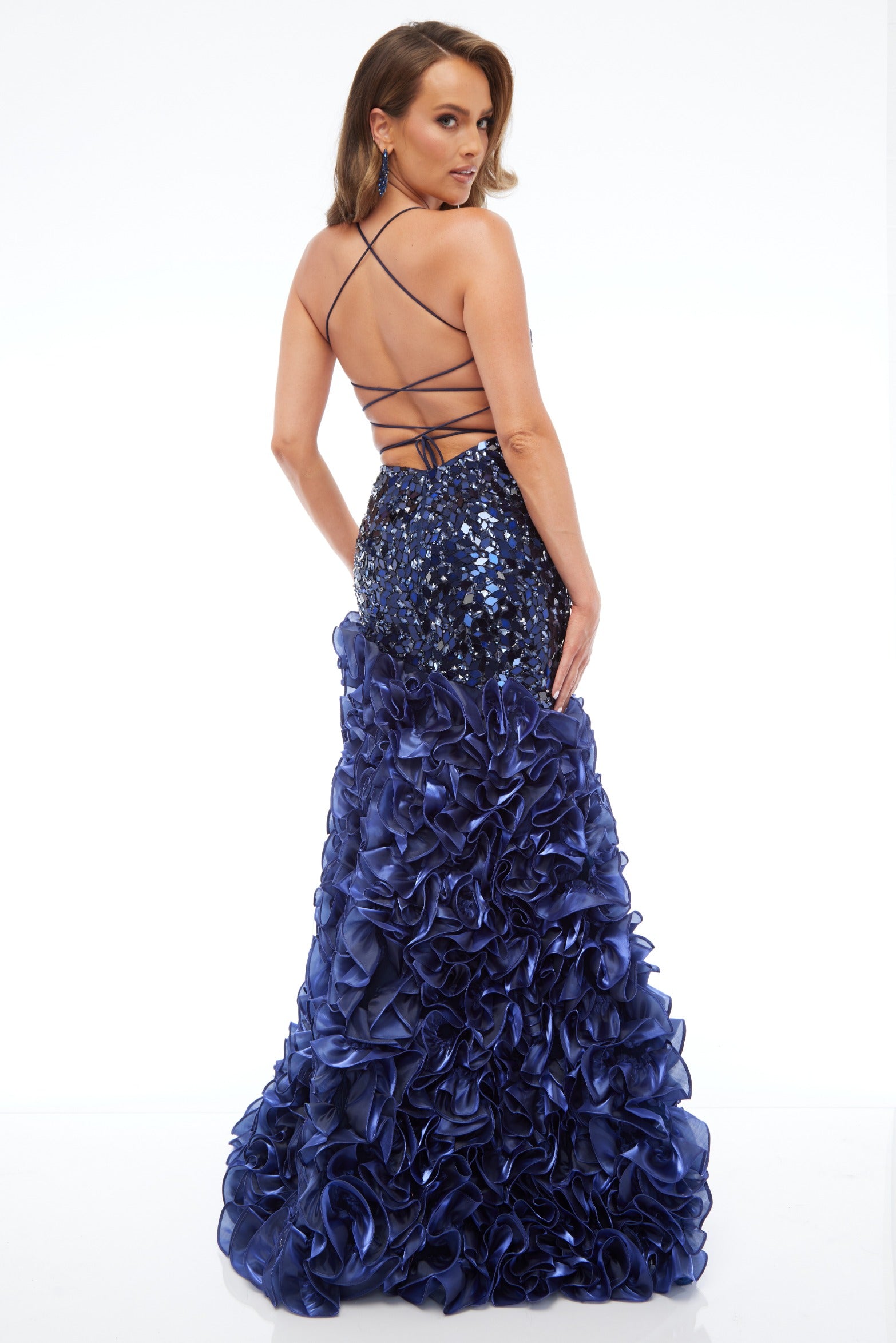 Back view of radiant fitted navy prom dress with stunning mirror details, ruffle skirt, and lace up back design. 