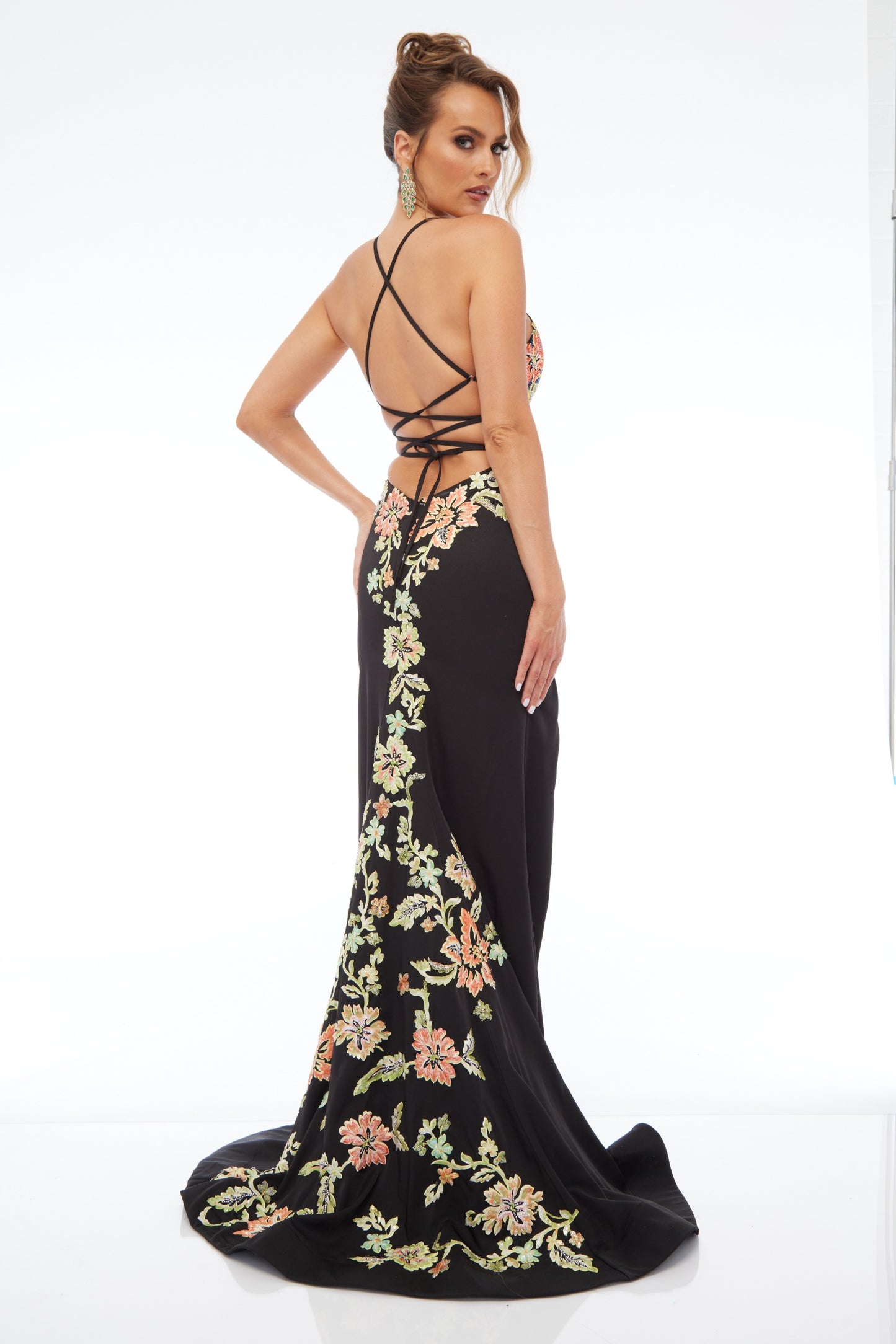 Back view of Style 7680: an enchanting black prom dress featuring detailed floral applique, high slit, lace up back, plunge neckline, and spaghetti straps.