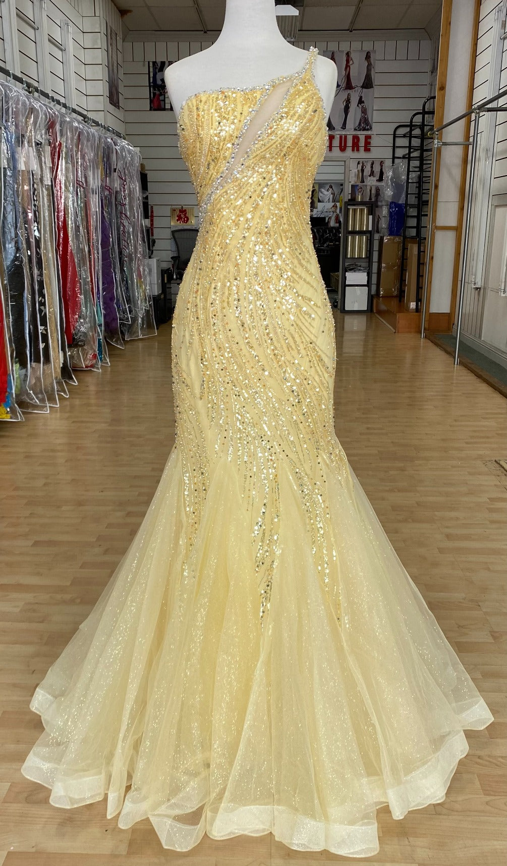 Front view of Style 7696: an enchanting fitted yellow prom dress featuring a beaded design, lace up back, one shoulder, and tulle skirt. 